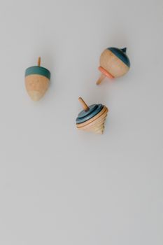 Three vintage wooden spinning tops in pastel colors on a soft white surface.