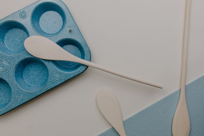 Minimalist flat lay of baking tools and blue muffin tray on light surface.