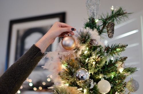 Free A hand decorates a Christmas tree with shiny ornaments, capturing the festive spirit. Stock Photo