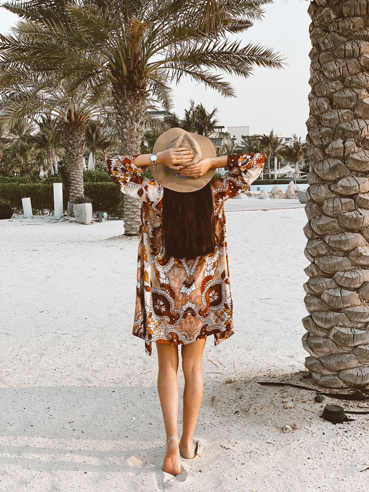 Back view of a woman in a straw hat on the sandy shore near palm trees