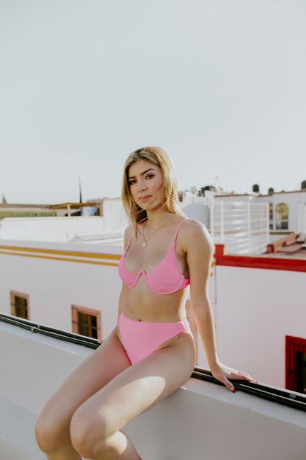 A young woman in a pink bikini sits on a rooftop, enjoying a sunny day.