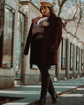 A fashionable woman poses on a Tehran street wearing a black coat and beret, embracing winter style.