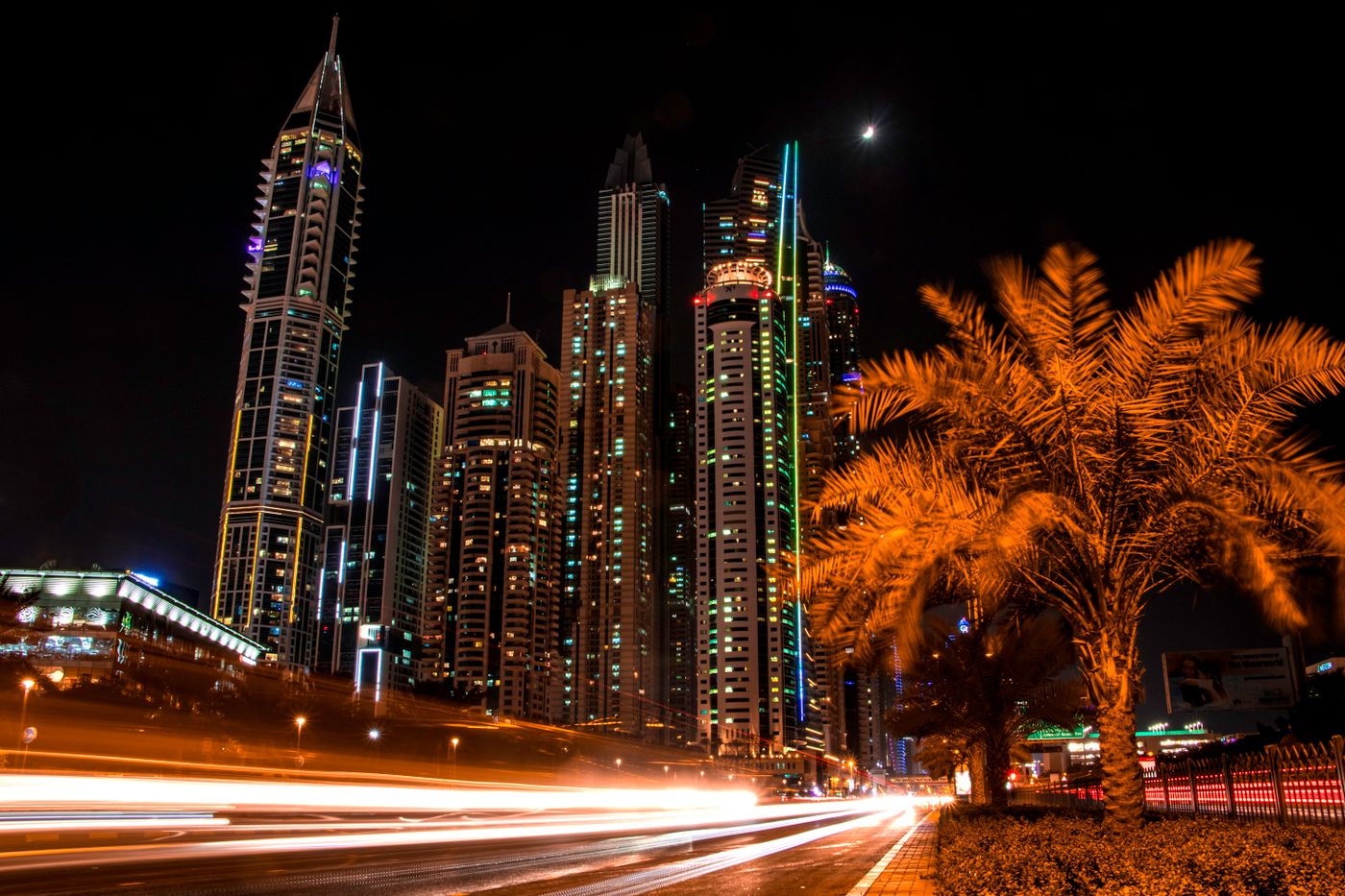 Dubai skyscrapers and palm trees at night with light trails from passing cars