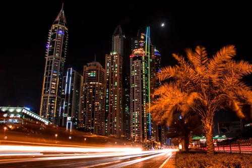 Free Stunning night view of Dubai's illuminated skyscrapers and palm trees with light trails from passing cars. Stock Photo