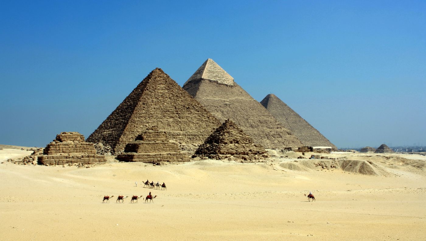 The Pyramids of Giza under a clear sky with camels in the desert foreground