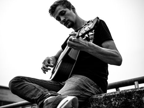 A thoughtful guitarist plays an acoustic guitar outdoors in black and white.