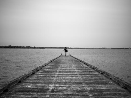 Free Grayscale Photo of a Guitarist Walking on a Wooden Dock Stock Photo