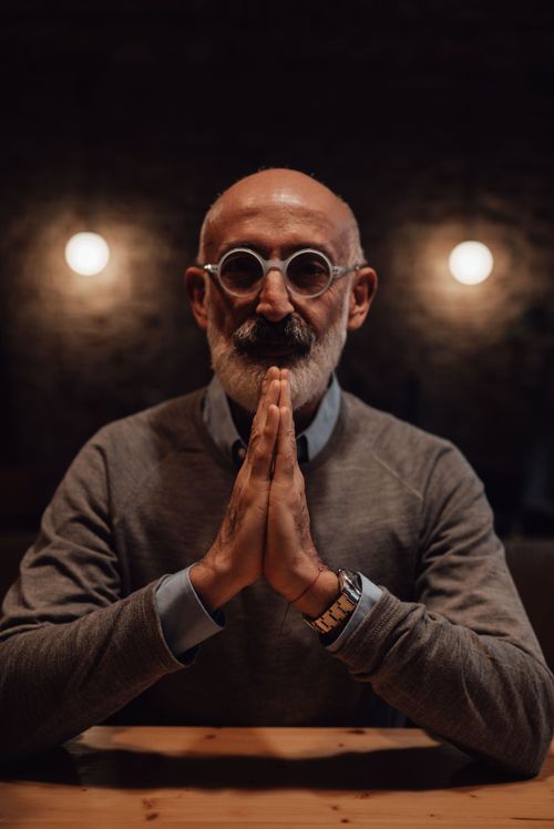 Free Tranquil senior male with beard and eyeglasses wearing elegant clothes looking at camera while sitting at table with folded hands Stock Photo