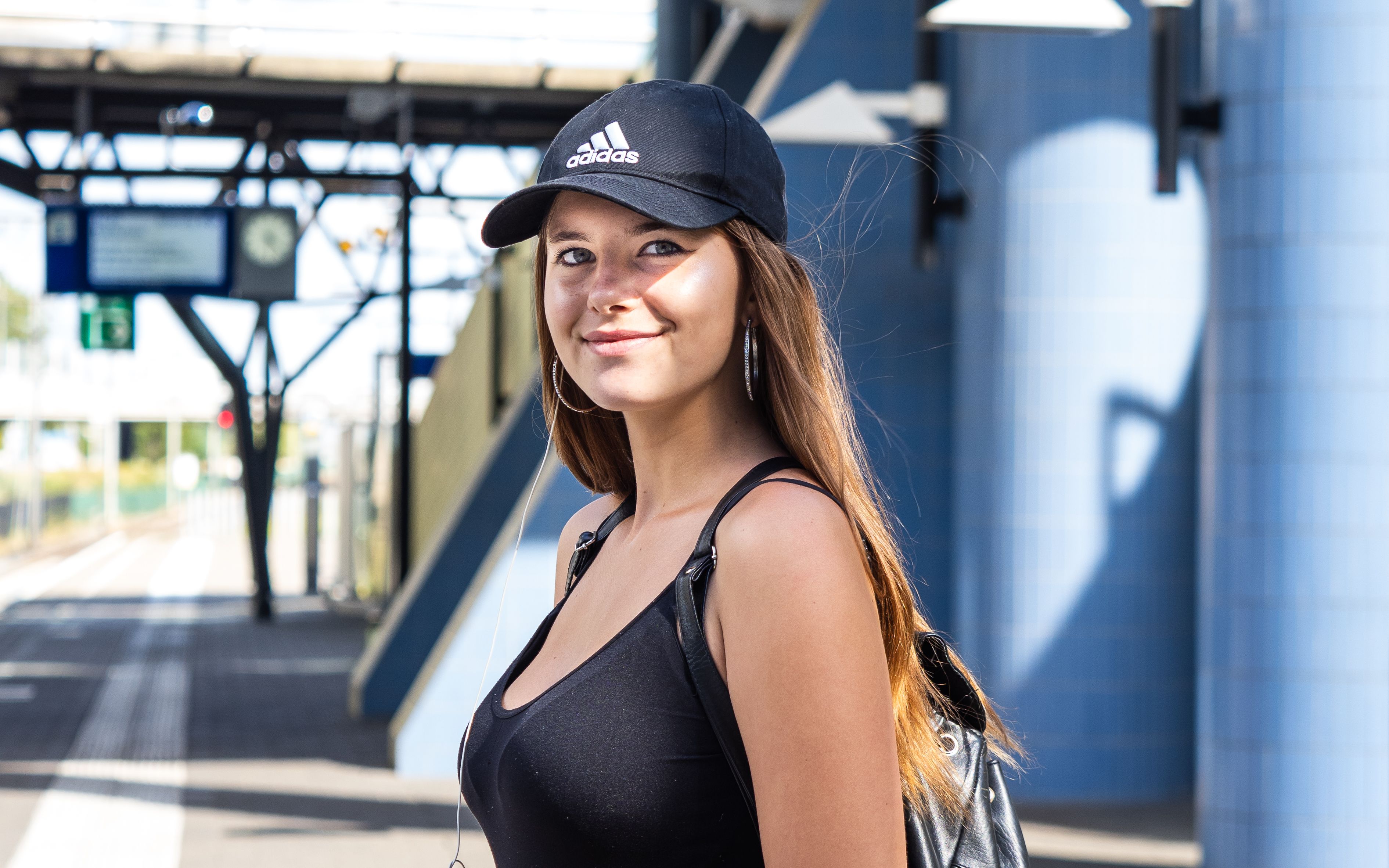 Confident young woman in casual wear smiling at a train station platform on a sunny day.