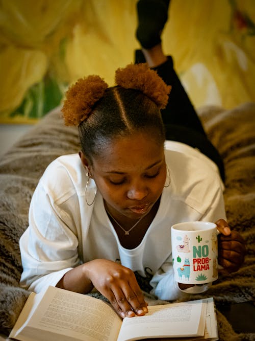 Free A Woman Reading a Book on the Bed While Drinking from the Mug Stock Photo