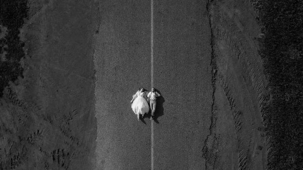 Aerial view of couple in wedding attire lying on road, symbolizing love.