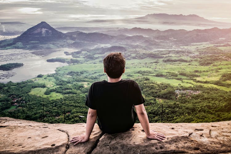 Back View Of A Man In Black T-shirt Sitting On Rock