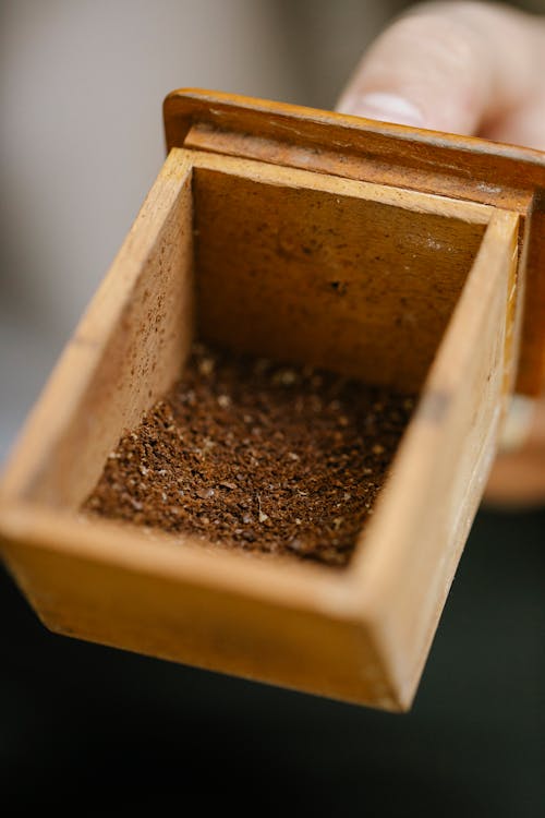 Crop anonymous person showing small wooden container with aromatic coffee powder on blurred background