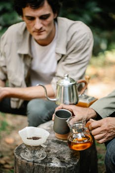 Two people brewing coffee outdoors using a pour-over method on a wooden stump.