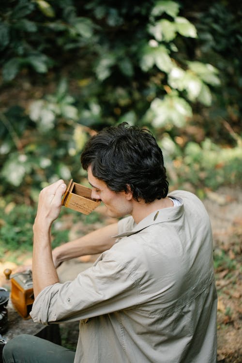 Side view of male in shirt enjoying ground coffee aroma in grinder box on blurred background
