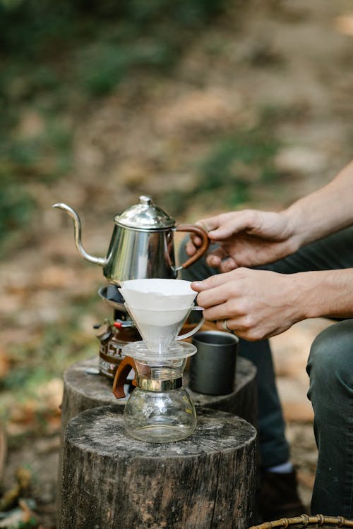 Crop man with kettle preparing coffee outdoors