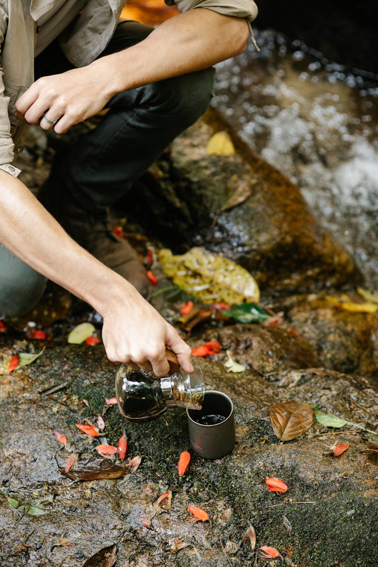 Man Pouring Coffee Into Metal Cup Near Clean Brook