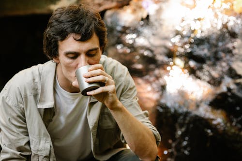Free Calm male relaxing and having cup of tea on blurred background of clean stream Stock Photo