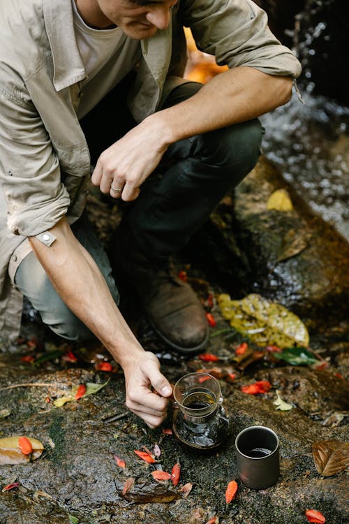 Free From above of crop young male hiker in casual clothes sitting on haunches and preparing coffee in chemex coffeemaker during trekking in autumn forest Stock Photo