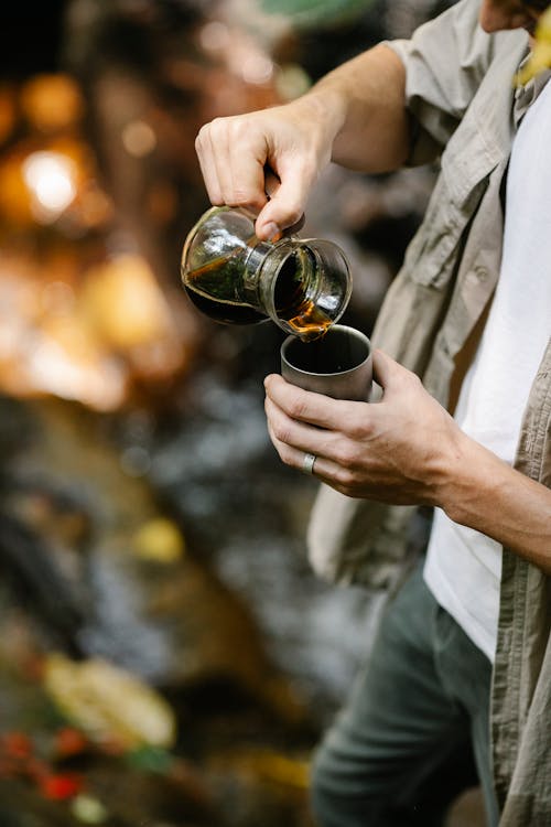 Free Crop male camper pouring coffee into mug in forest Stock Photo