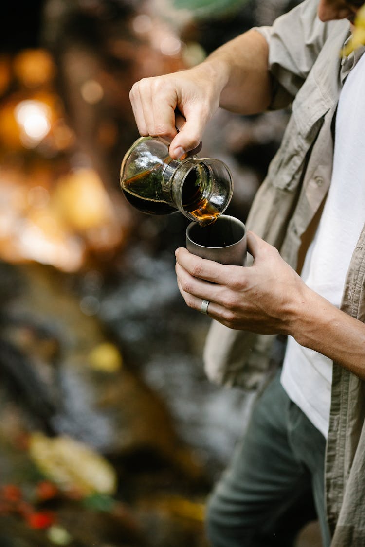 Crop Male Camper Pouring Coffee Into Mug In Forest