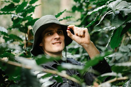 Happy young male farmer smiling and looking at small ripe red berry while working in lush green garden