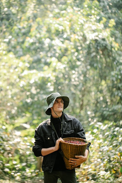 Free Satisfied young male farmer standing in garden with basket of harvested berries Stock Photo