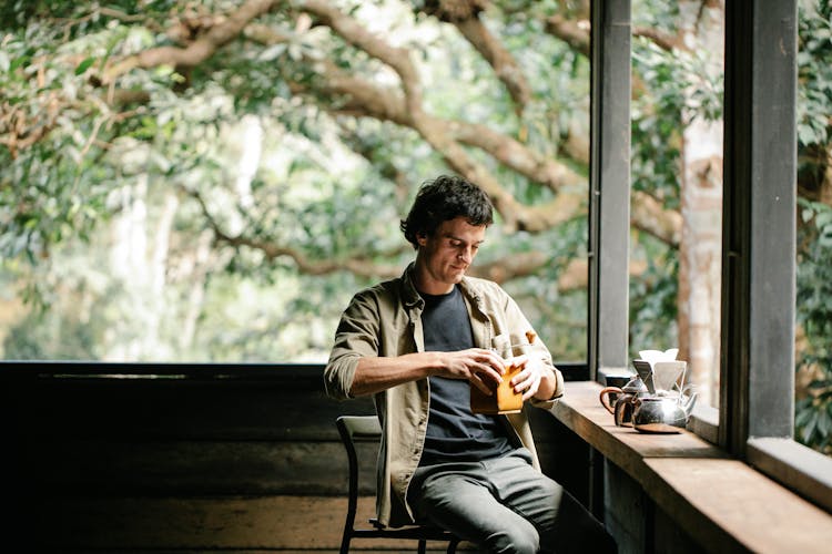 Man Milling Coffee In Grinder Against Kettles On Veranda