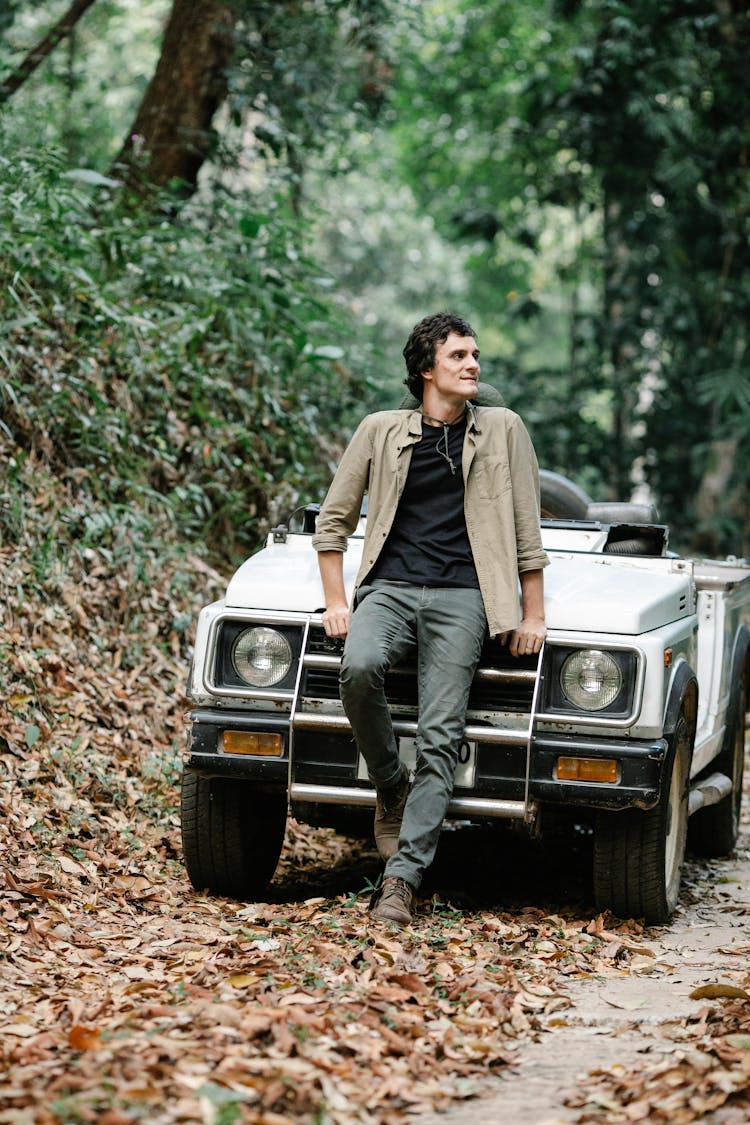 Confident Young Man Leaning On Car And Looking Away In Autumn Forest