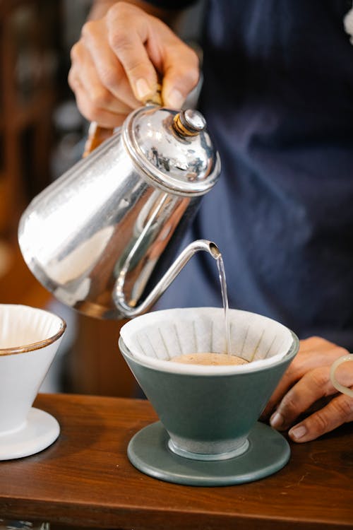 Free Crop anonymous male barista filling hot water from metal kettle into cup while preparing aromatic pour over coffee in cafe Stock Photo