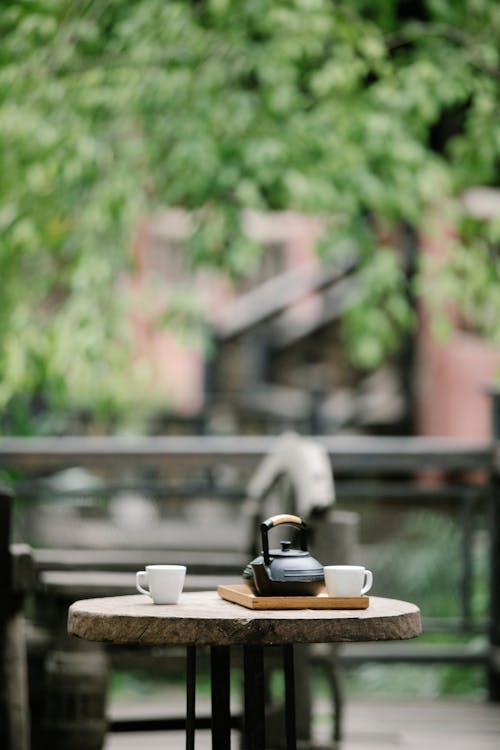 Free Ceramic cups and pot served on wooden tray on small round table on terrace of cafe in daytime Stock Photo