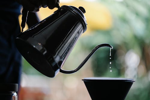 Crop faceless person filling water from kettle while brewing pour over coffee