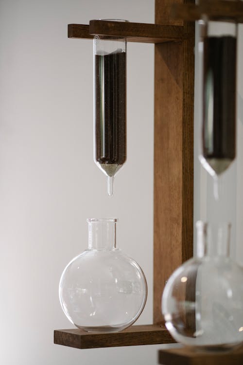 Ground coffee in transparent flask above glass carafe during brewing with Kyoto dripper against white background