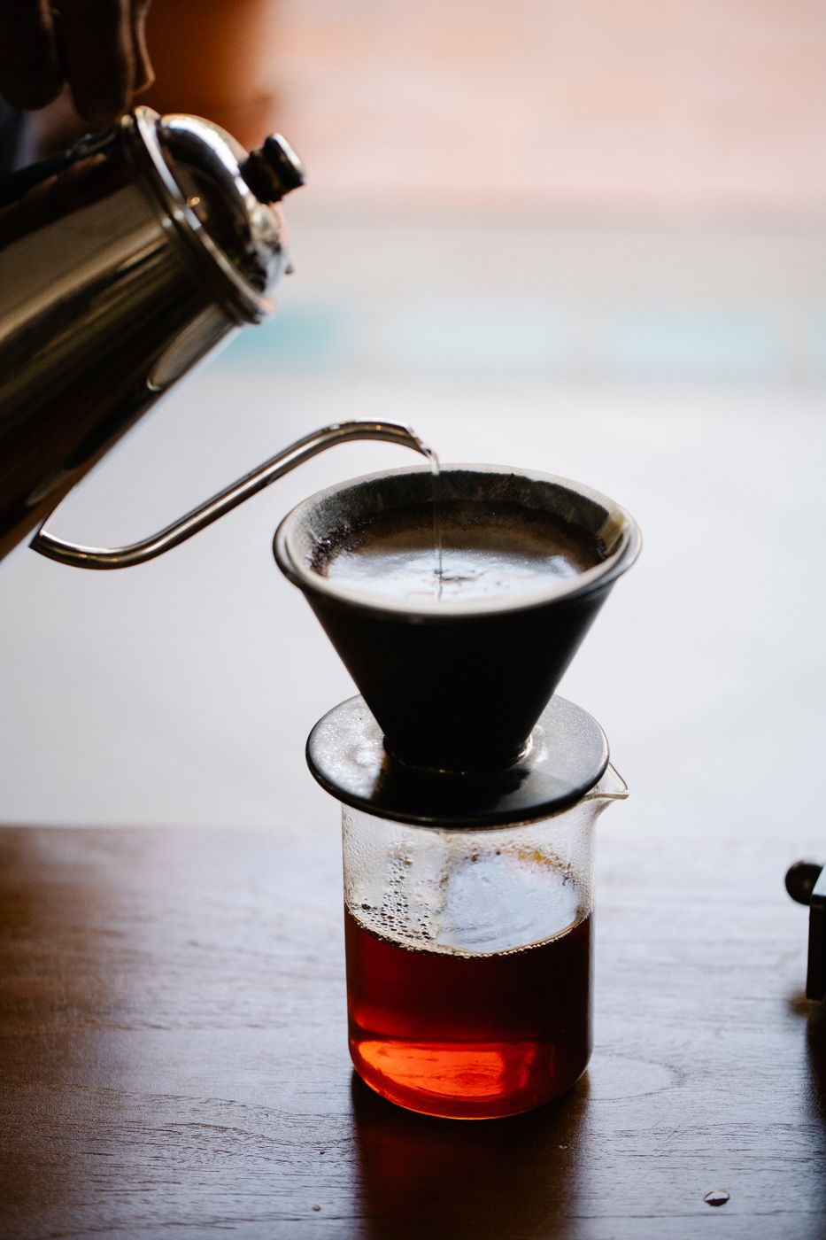 A hand pouring water in a slow spiral over freshly-ground coffee in a ceramic pour-over dripper, steam rising