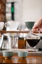 Crop anonymous barista pouring freshly brewed coffee from glass pot into mug in coffee shop with drippers on blurred background