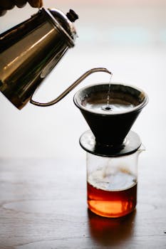 Pouring hot water over coffee grounds using a dripper and kettle in a café.