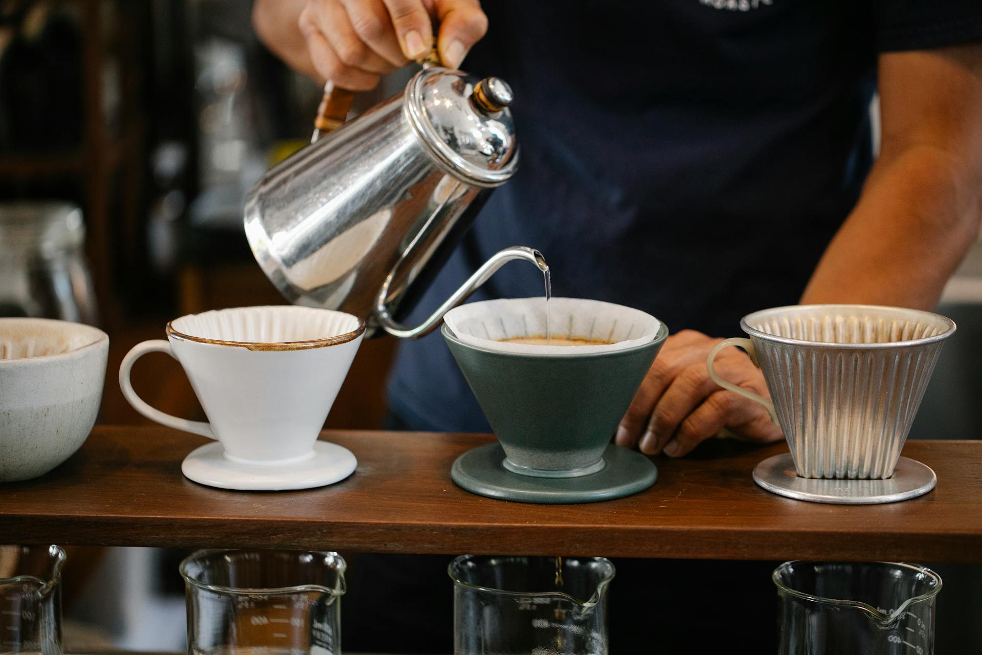 Barista pours water for pour over coffee in a café, using a gooseneck kettle.