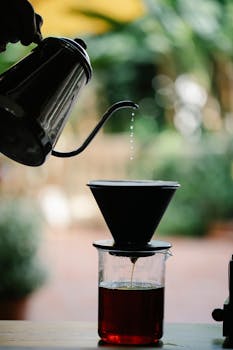 Silhouette of a kettle pouring hot water over coffee grounds using a filter dripper.