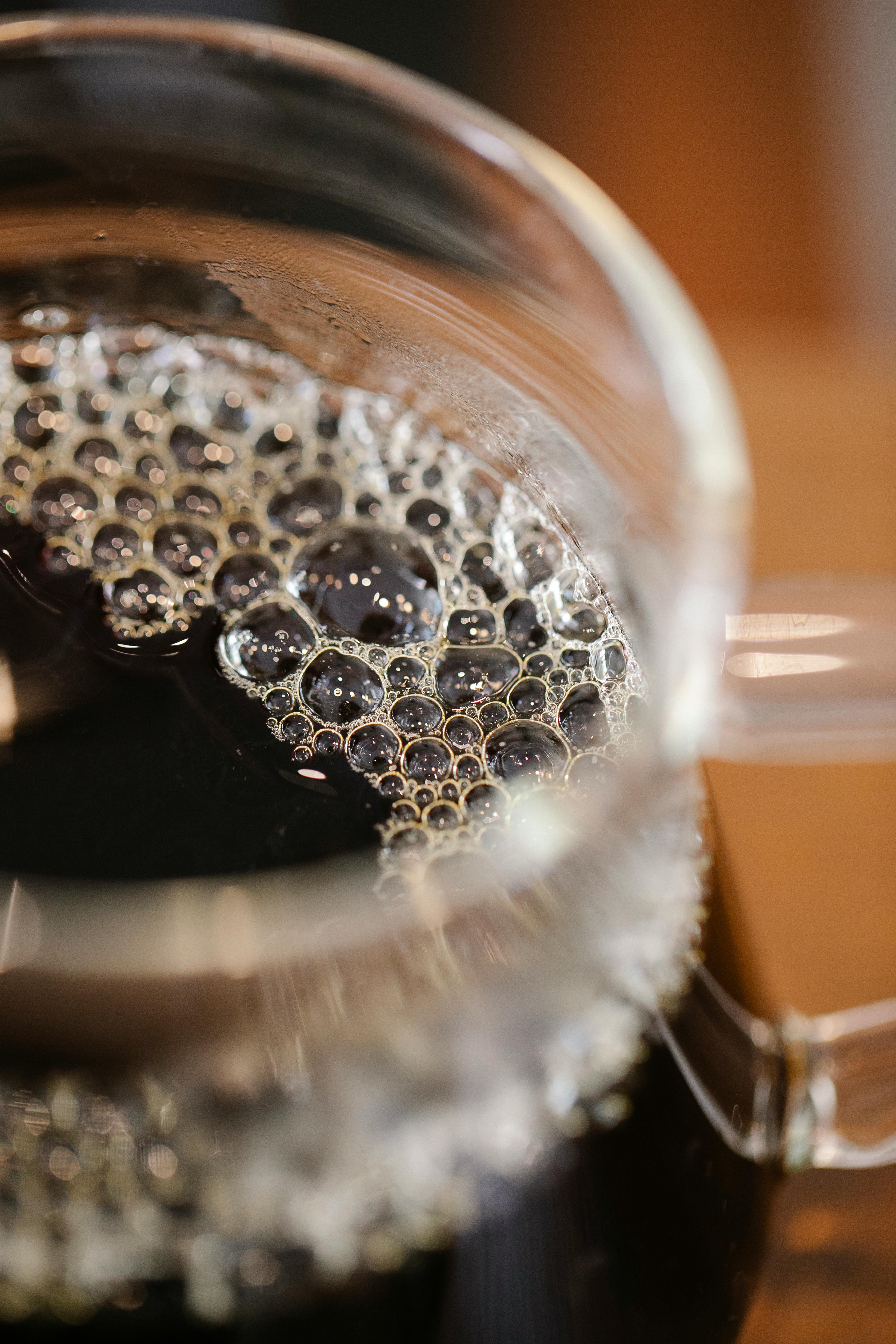 Closeup of glass cup with freshly brewed tasty coffee with bubbles placed on table in modern cafe on blurred background