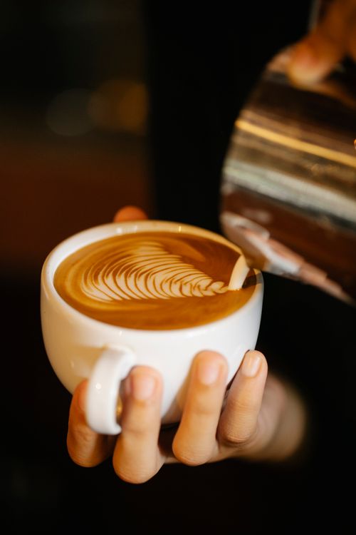 Free Crop unrecognizable barista pouring frothy milk from pitcher into cup of freshly brewed latte with ornament while working in cafe Stock Photo