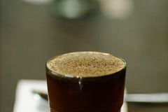 Glass cup of freshly brewed coffee with froth placed on table with spoon and piece of paper with numbers on blurred background during cupping