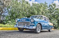 一辆经典蓝色汽车，带有镀铬细节，停放在郁郁葱葱的绿色背景的室外