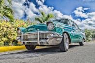 在古巴哈瓦那一条阳光明媚、绿树成荫的道路上，一辆修复精美的老爷车驶过，天空充满活力