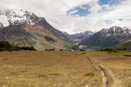 Free Explore a scenic mountain valley with a dirt path leading into the rugged landscape under a partly cloudy sky. Stock Photo