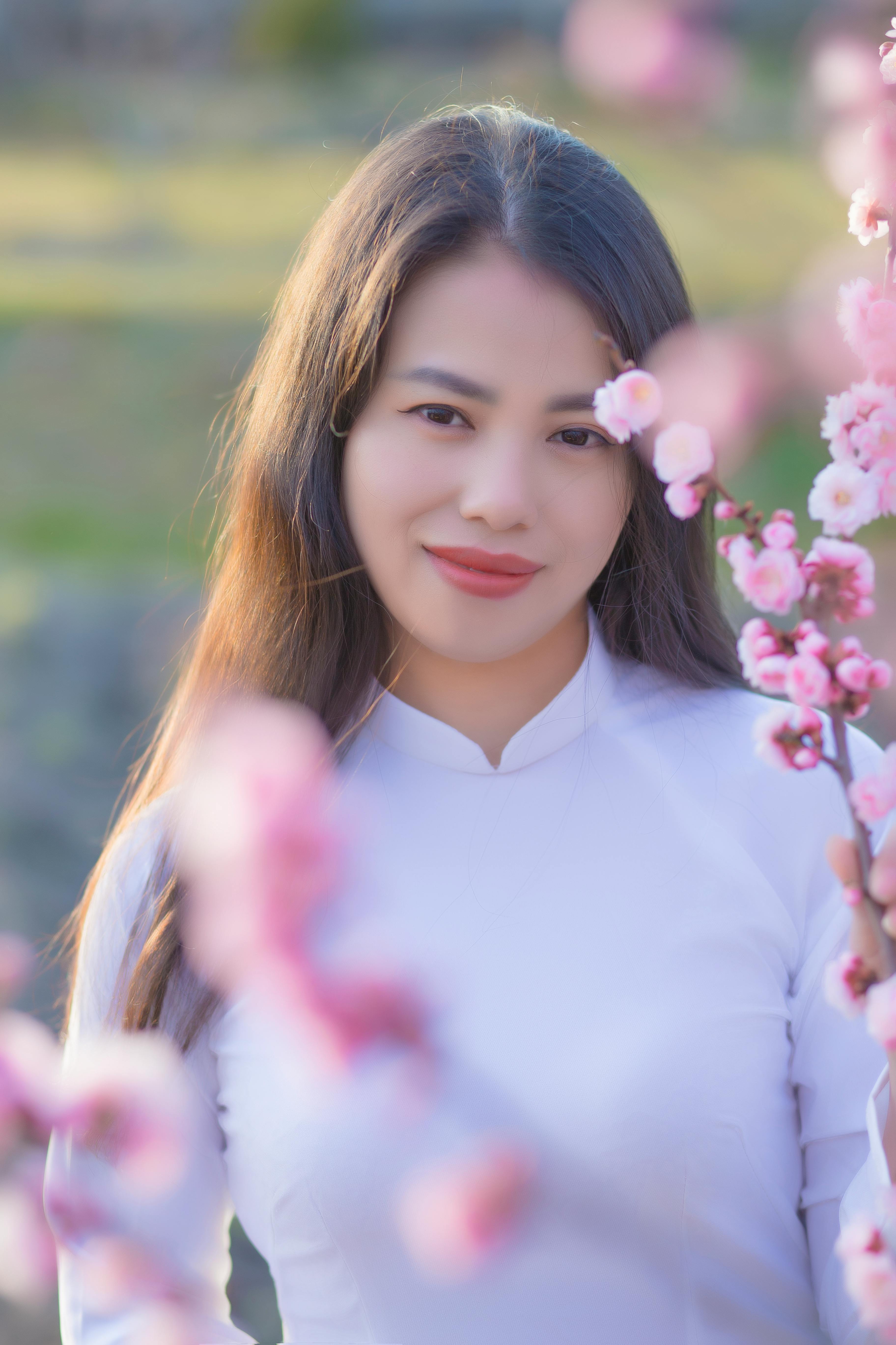 A peaceful portrait of a woman with pink blossoms framing her face outdoors.