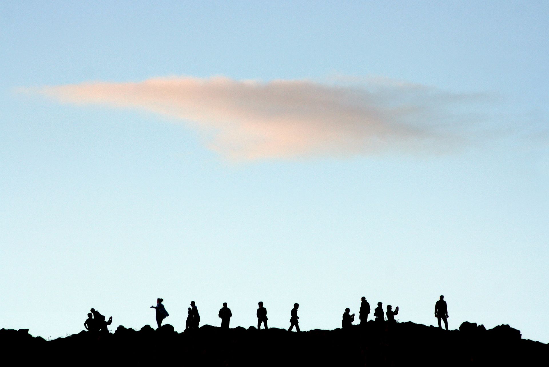 A silhouette of people gathered on a hill with a clear blue sky and cloud overhead.