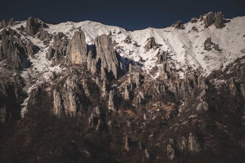 Rough rocky mountain range with uneven surface covered with white snow located in highlands on cold winter day in nature