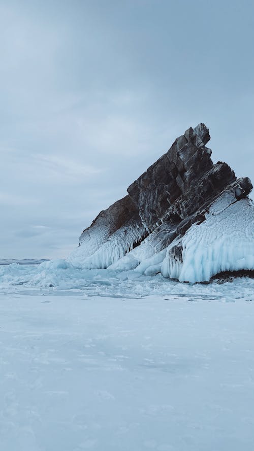 Snow Covered Rock Formation Under White Clouds