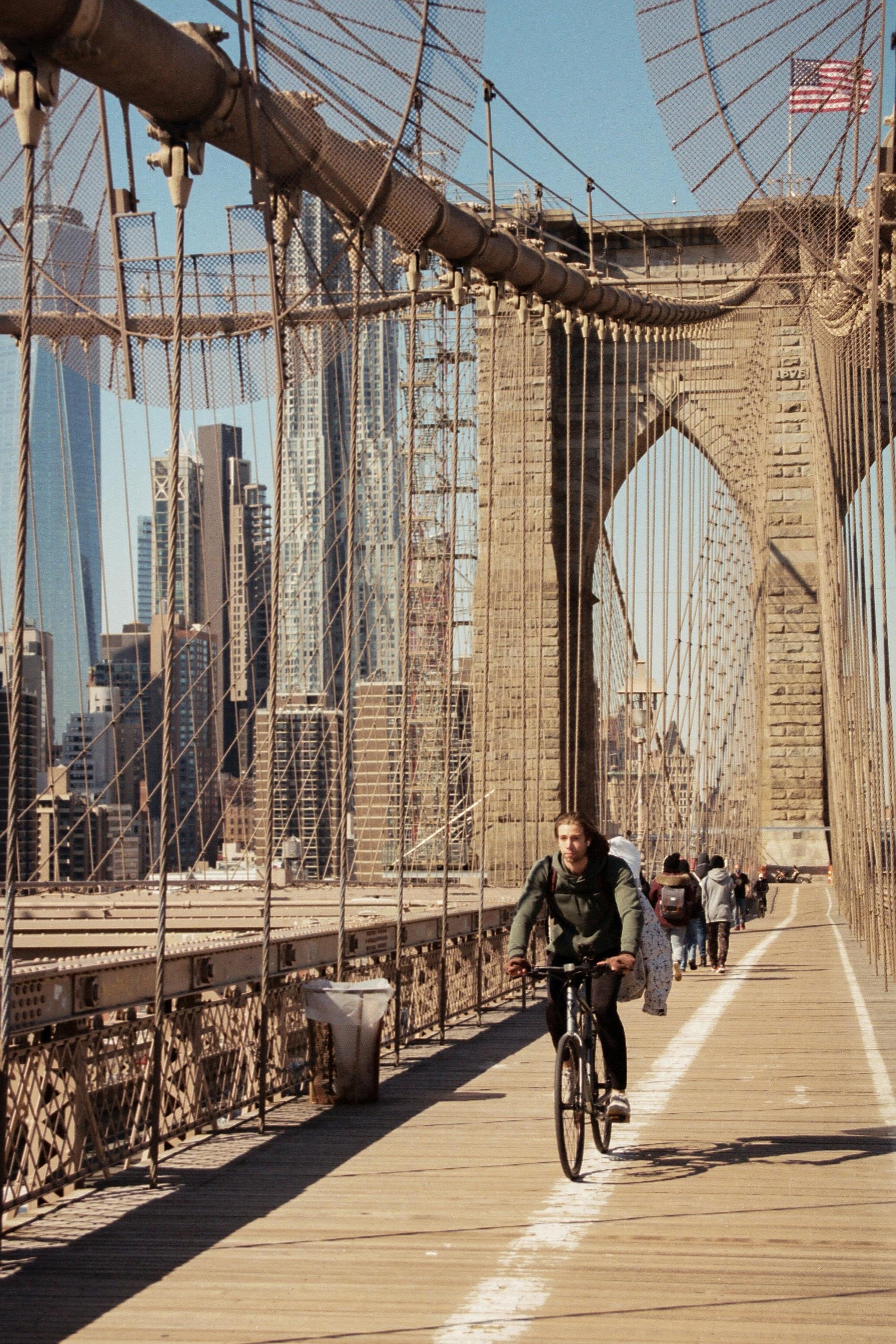 Man cycling over the iconic Brooklyn Bridge with New York City skyline in the background.