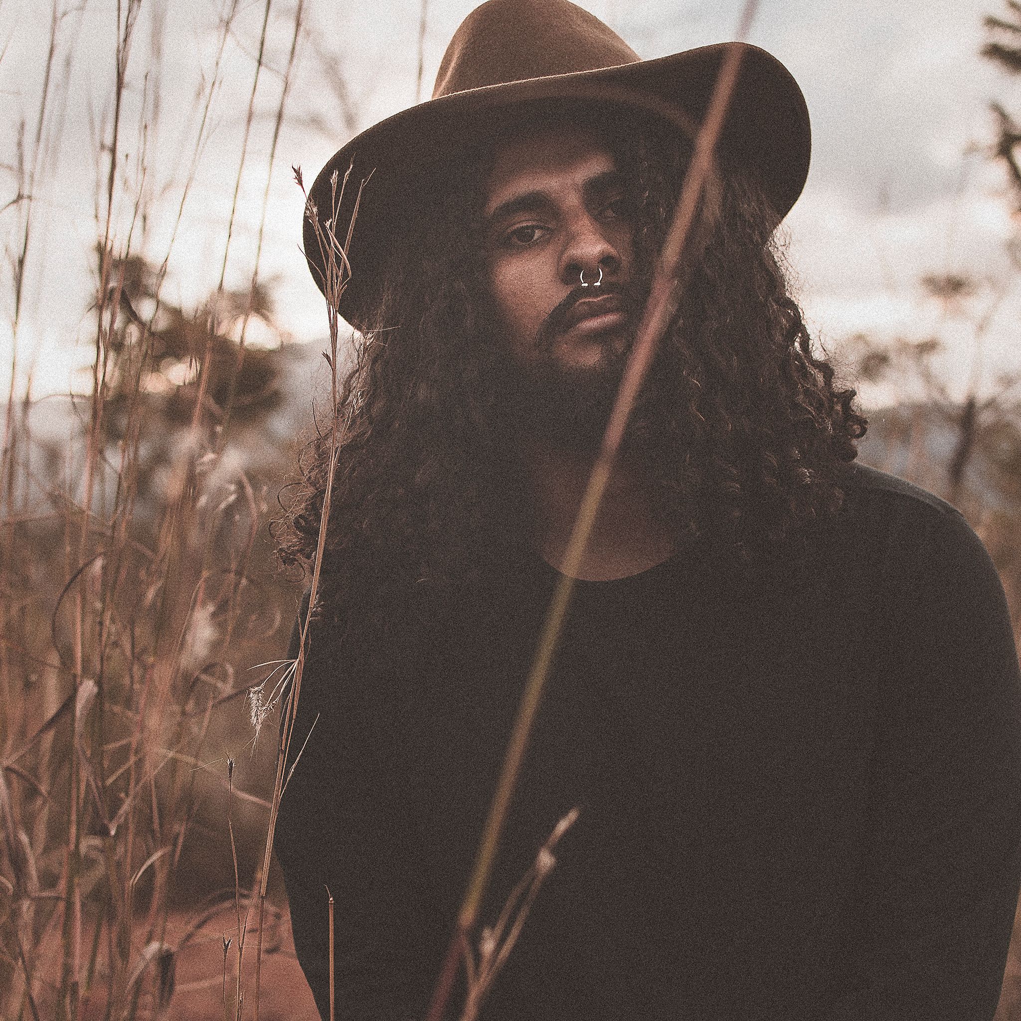 A striking portrait of a man with curly hair and hat in a natural outdoor setting.